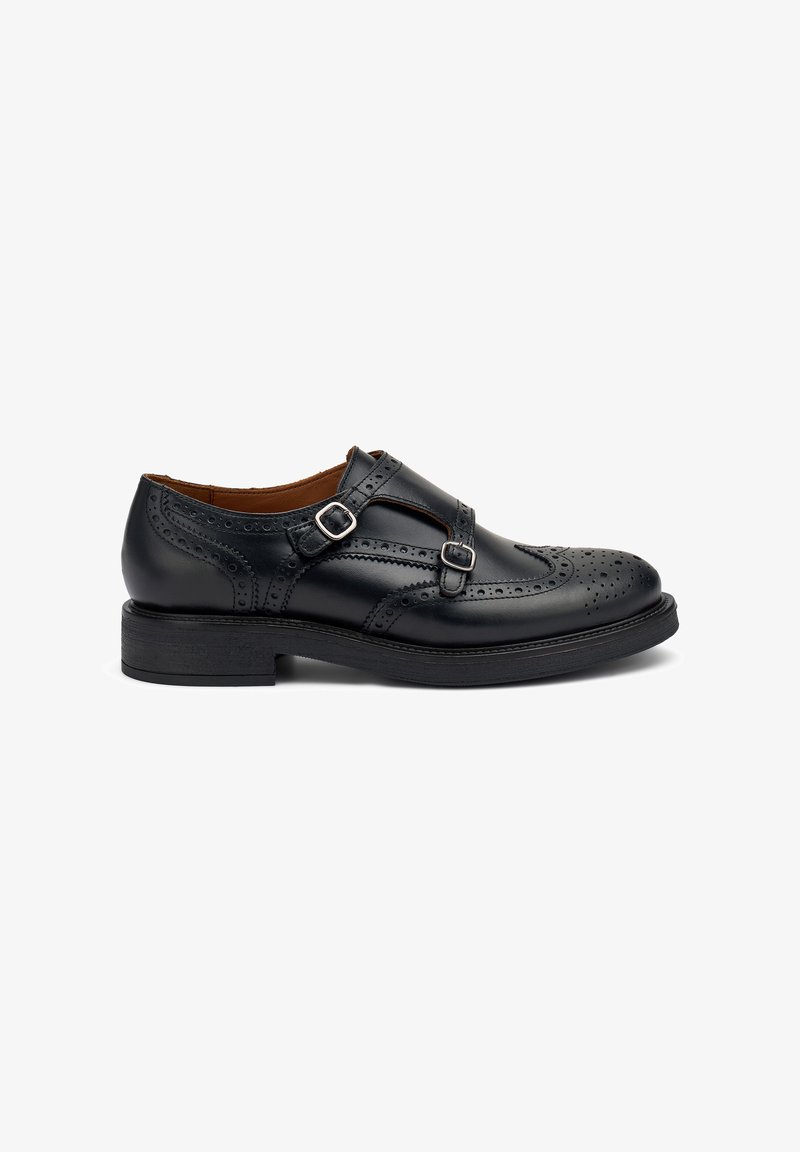 Zapato de cuero negro con detalles de brogue, dos correas ajustables con hebillas de plata y una suela de goma negra. Diseño clásico, tacón bajo.