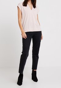 Ljusrosa V-ringad topp med korta ärmar, ihop med svarta raka jeans och svarta ankelstövlar. Slät tyg och avslappnad passform.