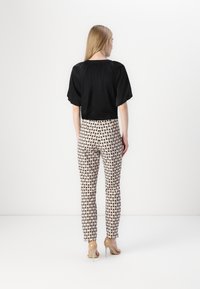 Black, short-sleeved top paired with patterned, beige and black, fitted pants. The pants feature a diamond design and are ankle-length.