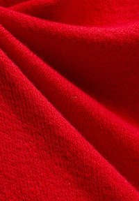 Gros plan d'un tissu tricoté doux de couleur rouge vif montrant une texture détaillée et des plis.