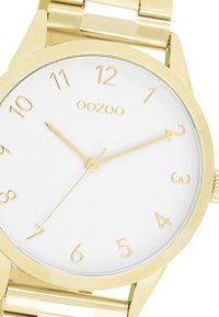 Montre-bracelet en or avec un boîtier rond, un cadran blanc, de grands index horaires en or et un design minimaliste. Dotée d'un bracelet en métal à maillons pour le fermoir.