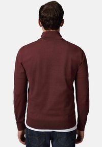 Maronenfarbener Strickpullover mit strukturiertem Muster, hohem Kragen, geripptem Saum und langen Ärmeln, über einem weißen Hemd getragen, von hinten gesehen.
