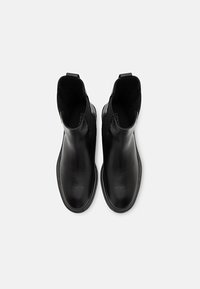 Botas negras de cuero hasta el tobillo con paneles laterales elásticos, textura suave, punta redonda y un diseño minimalista. Suelas de goma planas.