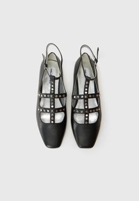Zapatos de cuero negros con un diseño abierto, detalles con tachuelas, un pequeño tacón y una plantilla plateada en contraste. Punta cuadrada.