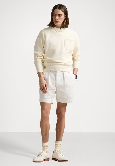 Hanorac crem cu buzunar, pantaloni scurți albi, pantofi crem și șosete bej. Casual, material moale. Design simplu cu accente minime.