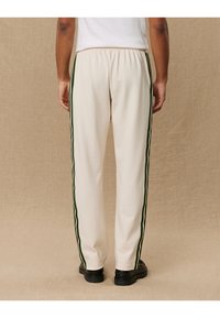 Cream-colored pants with dark green side stripes, elastic waistband, and straight-leg cut. Material appears smooth and slightly shiny.