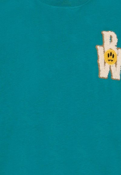 Turkusowa tkanina z białymi, teksturowanymi literami „B” i „W” oraz małą żółtą okrągłą łatką z smutną buźką pomiędzy literami.