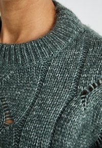 Maglione di lana con collo a girocollo rigato, caratterizzato da un motivo testurizzato in verde teal smorzato e piccoli fori per un tocco di dettaglio in più.