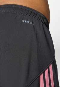 Czarne szorty sportowe o gładkiej fakturze, z różowymi akcentami wzdłuż boków i elastycznym pasem z logo "AEROREADY".