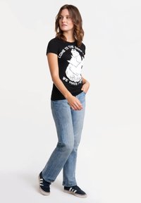 Black cotton t-shirt featuring a graphic design in white text and illustrations, paired with light blue jeans and black sneakers.