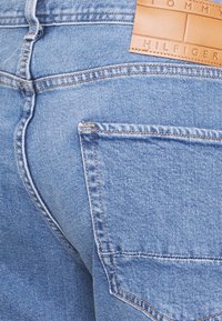 Vaqueros de mezclilla azul claro con un bolsillo trasero, con costuras claras y una etiqueta de cuero marrón con la inscripción "Tommy Hilfiger" en relieve.