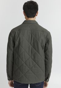 Olivově zelená prošívaná bunda s límcem, knoflíkovými manžetami a diamantovým vzorem. Vyrobena z odolné tkaniny, má rovný střih a zádové švy.