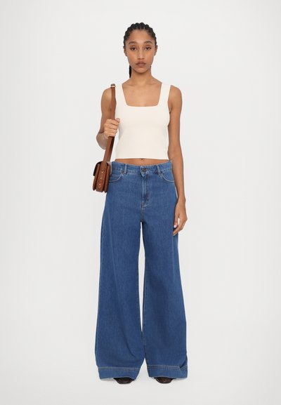 Wide-leg blue denim jeans with a high waist, paired with a fitted cream tank top. Brown crossbody bag adds contrast. Clean, modern silhouette.
