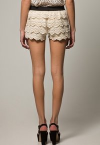 Spetsbyxor med vågig nederkant, ljusbeige färg, texturerad design och svart midjeband. Matchas med svarta högklackade sandaler.