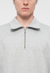 Harmaa vetoketjullinen collegepaita, joka on valmistettu pehmeästä kankaasta. Sitä koristaa metallinen vetoketju ja rento malli. Sujuva pinta koko ajan.