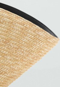 Vævet stråkurv med en kegleformet design, naturlig beige farve med struktureret overflade, og en kontrasterende sort kant langs den øverste kant.