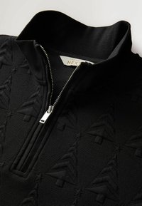 Sort tekstureret sweater med præget juletræsmønster og delvis åbnet sølvlynlås på ståkraven.