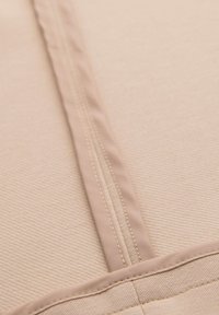 Gros plan d'un tissu beige avec une couture centrale et un ourlet cousu, montrant la texture et les détails des fils.