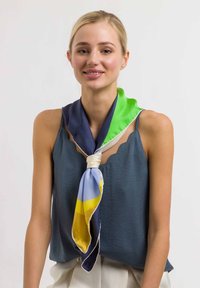 Svila šal z gradientom zelene, mornarsko modre in modre barve z rumenimi detajli, elegantno vezan okoli vratu, na modelu, ki nosi preprost rjuh.
