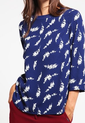 Navyblå bluse med hvidt abstrakt blomstermønster, rund halsudskæring, trekvartærmel og blød stoftekstur.