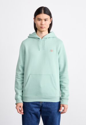 Sudadera con capucha de un suave tejido en color verde menta claro, con un bolsillo tipo canguro en la parte frontal, puños acanalados y un pequeño parche con el logo en el pecho.