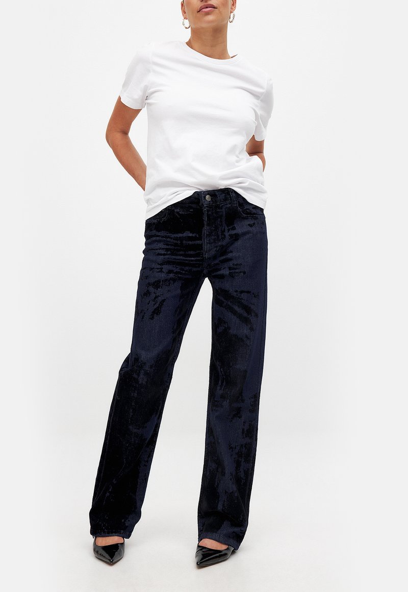 White crew-neck t-shirt paired with dark navy wide-leg velvet pants. Pants feature a smooth texture, front pockets, and button closure.