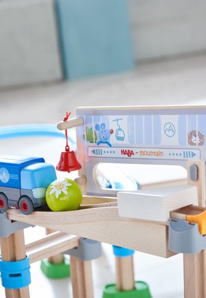 Wooden toy playset with a blue truck, green ball with a flower design, red bell, and a lift-themed backdrop featuring cartoon animals.