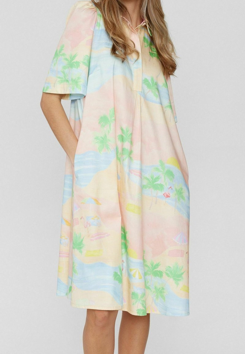 Robe à manches courtes avec un imprimé pastel tropical de plage comprenant des palmiers, des flamants roses et le soleil, fabriquée en tissu léger.