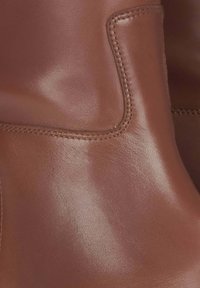 Brązowe skórzane buty za kostkę o gładkiej fakturze, zaokrąglonych krawędziach i widocznym przeszyciu. Minimalistyczny design z bocznym wycięciem.