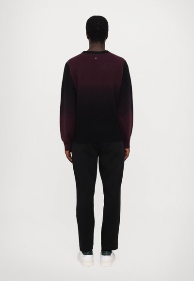 Pulover cu model gradient în nuanțe de burgund și negru, cu mâneci lungi și guler rotund. Asortat cu pantaloni negri și adidași albi.