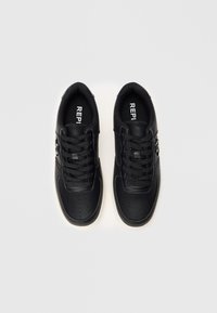 Paire de baskets noires en cuir avec lacets et détail de boucle latérale, vue de dessus sur fond blanc.