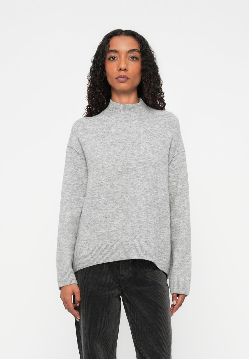 Maglione grigio lavorato a maglia con collo alto, vestibilità ampia, orlo a coste e spalle cadenti, abbinato a pantaloni in velluto a coste scuri.