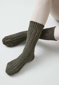 Calzini lavorati a maglia di un verde scuro con una texture a coste e un polsino spesso. Il materiale presenta leggere variazioni di colore, che ne esaltano l'aspetto robusto.
