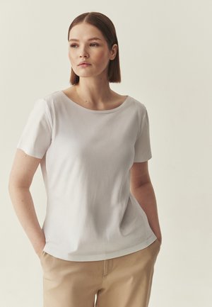 White short-sleeve t-shirt with a rounded neckline and soft texture, featuring a relaxed fit. Paired with beige trousers.
