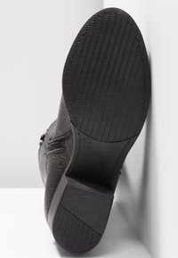 Semelle de botte noire avec motif de bande de roulement en zigzag, talon bas carré et fermeture éclair latérale visible sur dessus en cuir texturé.