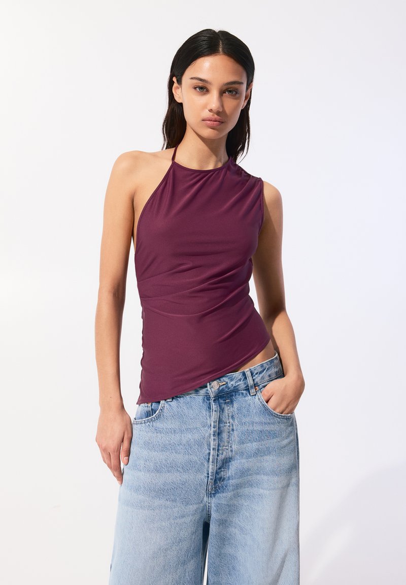 Haut halter bourgogne avec une silhouette ajustée et une texture douce, associé à un jean décontracté en lavage clair. Pas de motifs ni de pièces métalliques visibles.