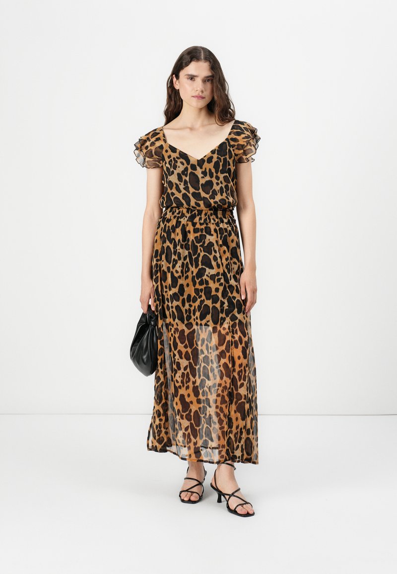Sukienka maxi w wzór panterki z przezroczystymi, falbaniastymi rękawami, elastyczną talią i zwiewnym materiałem. Zestawiona z czarnymi sandałami na szpilce i torebką.