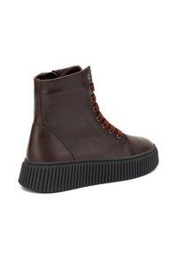 Botín de cuero marrón con cordones marrones, ojales dorados y suela de goma negra acanalada. Presenta una puntera redondeada y detalles de costura.