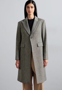 Houndstooth-patterned, gray wool coat with a notched collar, two front pockets, and a button closure, worn over a black top and beige pants.