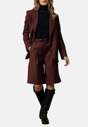 Blazer bordeaux su misura e pantaloni a pieghe abbinati, abbinati a un dolcevita nero e stivali neri sopra il ginocchio. Tessuto liscio e vestibilità strutturata.