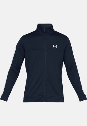 Veste de sport noire à fermeture éclair intégrale, col montant, manches longues, bande blanche le long des bras et logo Under Armour blanc sur la poitrine.