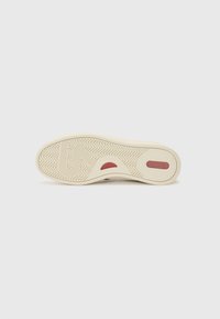 Schuhsohle in Creme mit einem strukturierten Muster und rotem Akzent. Gebogene Form mit einem Fischgrätenprofil für besseren Halt.