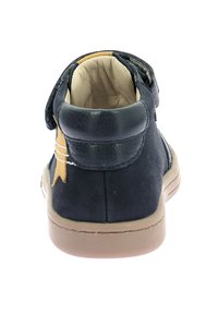 Stivaletti alla caviglia in suede blu navy con dettagli in pelle tan, cinturino con chiusura a strappo e suola in gomma texturizzata. Design minimalista, punta arrotondata.