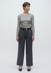 Ριγέ μπλουζάκι με μακριά μανίκια και λαιμόκοψη καραβιού, συνδυασμένο με ψηλόμεσο, φαρδύ γκρι παντελόνι και μαύρες γόβες με μυτερή μύτη.