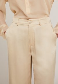 Krämfärgade, satinbyxor med flat front, bältesslingor, sidfickor och en enda knappstängning. Slät textur.
