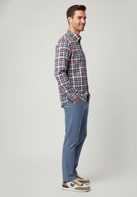 Camisa de cuadros de manga larga para hombre en colores azul, rojo y blanco, combinada con pantalones texturizados azul claro y zapatillas beige.