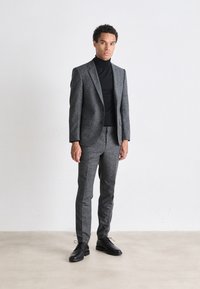 Completo in tweed grigio con vestibilità su misura, abbinato a un dolcevita nero e scarpe stringate nere. Texture liscia e modelli sottili evidenti.