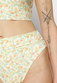 Blommig bikiniöverdel och högmidjade trosor med ribbad textur. Har små gula och rosa blommor mot en ljus bakgrund.