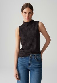 Black sleeveless top with a high collar and textured fabric, paired with light blue high-waisted jeans featuring five pockets.
