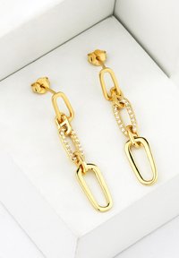 Guldtonade örhängen med länkade ovala former där en kedja accentueras av klara rhinestones, placerade mot en neutral presentlåda.